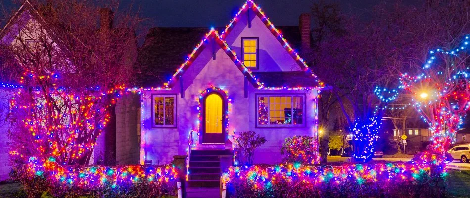 Colored Christmas lights on a house, trees, and shrubs in Ankeny, IA.