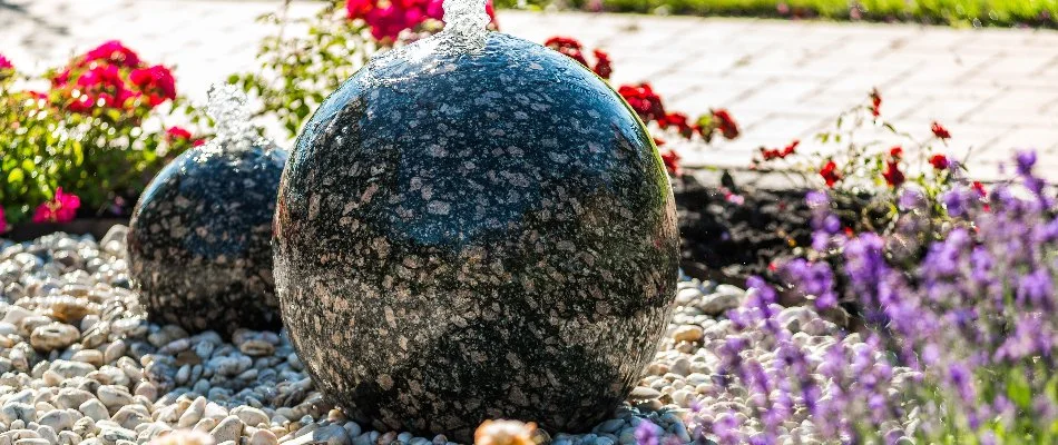 Core-drilled boulder water feature in Ankeny, IA, with rocks and flowers.