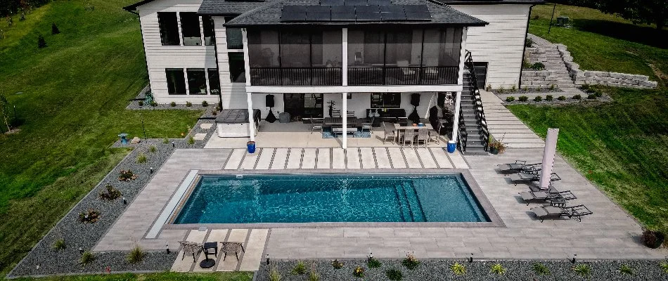 Aerial view of a modern home featuring a swimming pool, outdoor seating area, and solar panels, surrounded by landscaped greenery.