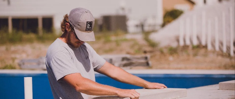 A contractor carefully working on the pool area, measuring and placing materials under the bright sun in Ankeny, IA.