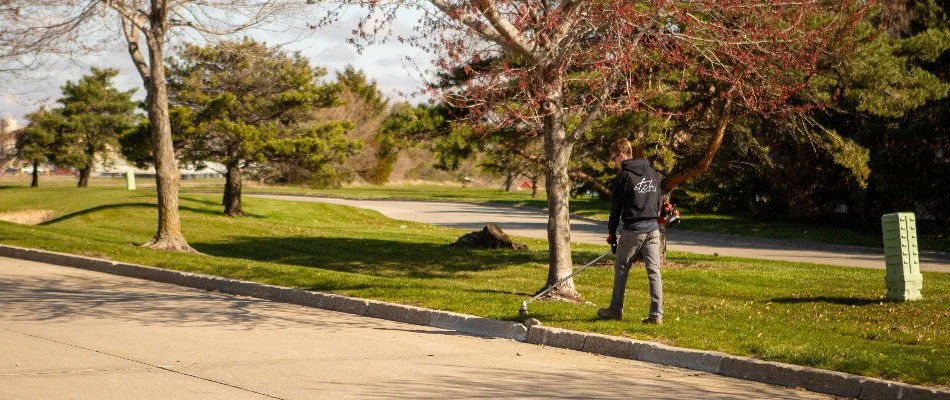 Worker trimming grass near curb on commercial property in Ankeny, IA.